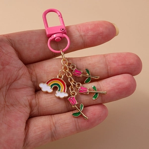 Chic rainbow cloud and pink rose metal keychain held in hand over beige background