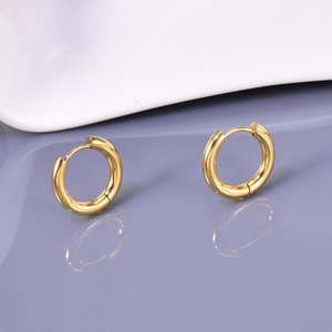 Polished gold titanium steel hoop earrings with reflective mirror effect on purple surface
