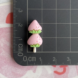 Detail view of pink strawberry resin charm with green leaves on a black measurement mat