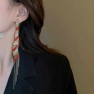Detail of long tiered tassel earrings with gold tubes and red beads worn by a model
