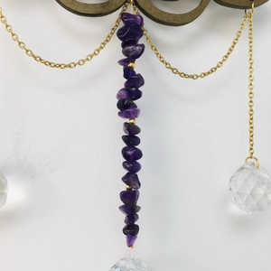 Detail of amethyst raw stones and crystal prisms hanging on golden chains suncatcher
