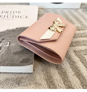 Vue détaillée d'un portefeuille rose en cuir avec nœud doré et compartiments pour cartes