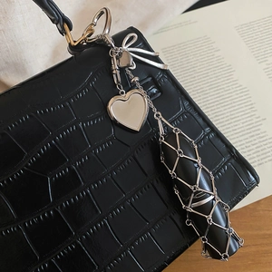 Detail of silver heart bow lipstick charm holder attached to a black crocodile texture handbag