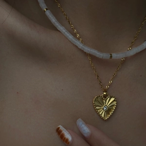 Close-up of layered gold heart pendant necklace and white beaded collar chain on neck