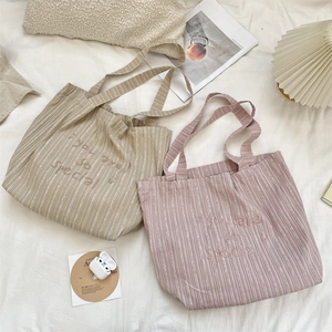 Detail of embroidered striped canvas tote bags in beige and pink with artistic text