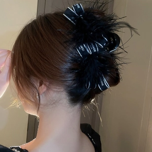 Detail of elegant black feather hair claw clip with printed ribbon in a chic hairstyle