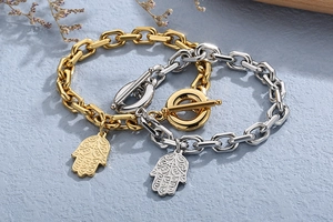 Detail of gold and silver chunky Hamsa hand bracelets with OT toggle closures on grey background