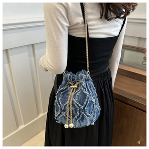 Detailed shot of denim bucket bag with frayed quilted texture and pearl chain drawstring