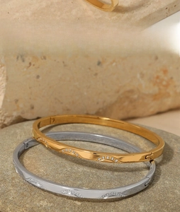 Macro detail of gold and silver wavy stainless steel bracelets with cubic zirconia on rocks