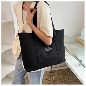 Close-up of black canvas tote bag with fashion label worn over the shoulder
