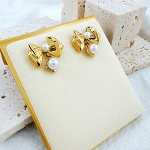 Detail of golden bow earrings with pearls displayed on a beige stone stand