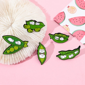Detail view of cute cat enamel pins shaped like green pea pods on a pink background
