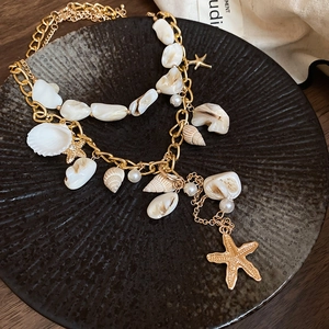 Macro detail of nautical layered necklace with golden starfish and natural seashell charms