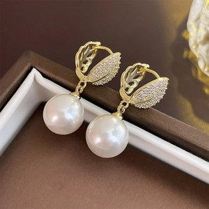 Close-up of gold-plated leaf earrings with sparkling zircons and glossy white pearls