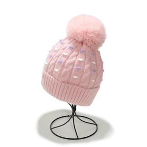 Detalle de un gorro de punto rosa con puntos de colores y pompón en un soporte