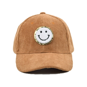 Makro-Detail des braunen Cordstoffs und des Pailletten-Smiley-Aufnähers auf der Kappe