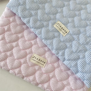 Detail of quilted heart pattern on striped fabric laptop sleeve with branded woven label