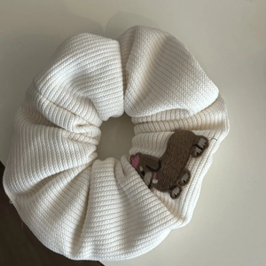 Close-up of cream knitted hair scrunchie featuring cute brown dog embroidery detail