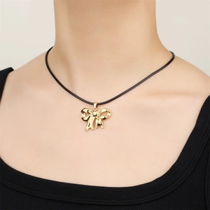 Close-up of a 18k gold-plated bow pendant worn on a black cord necklace by a model