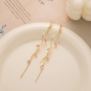 Elegant long leaf tassel earrings with gold branches and pink gems on a white plate
