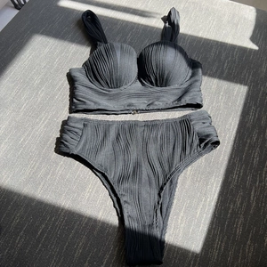 Detail of black pleated two-piece high-waisted bikini set with underwire cups and textured fabric
