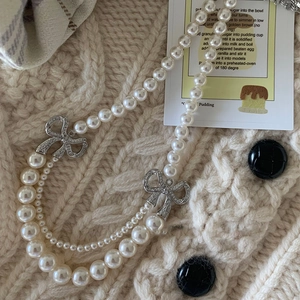 Collier de perles à double rangée avec nœuds en diamant étincelant sur un pull en maille