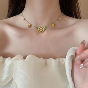 Detail of sunflower necklace with yellow enamel petals and green leaves on a gold chain