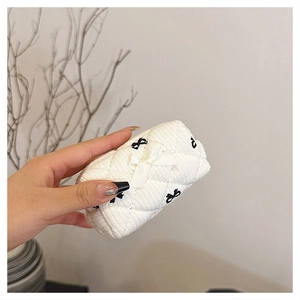 Close-up of a white quilted floral cotton makeup bag with black bow embroidery detail