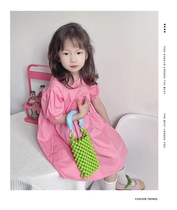 Ragazza in abito rosa con borsa di perline verde brillante e manici azzurri morbidi