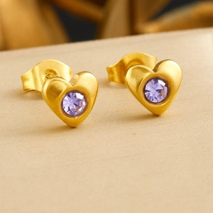 Boucles d'oreilles cœur en or 18k avec pierres zircon violettes sur fond beige