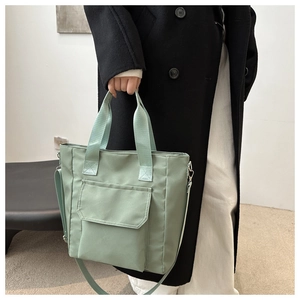 Detailed shot of a light green nylon tote bag featuring a front pocket and adjustable strap