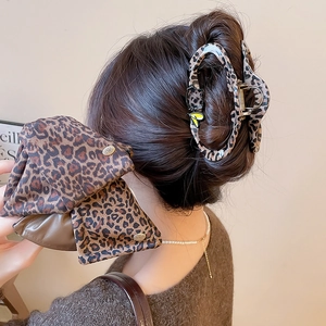 Detail view of a leopard print hair claw and fabric bow with elegant metallic accents