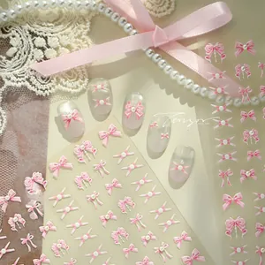 Macro view of 3D pink bow nail art stickers with pearls on lace background