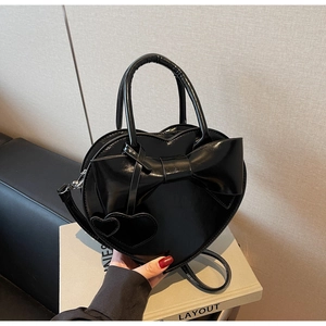 Détail du sac à main noir en forme de cœur avec un grand nœud et texture vernie