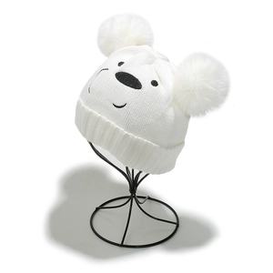 Détail du tricot d'un bonnet d'ours blanc pour bébé avec pompons et broderie noire