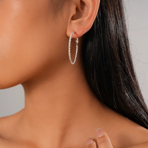Close-up of model wearing large silver twisted hoop earrings with a metallic finish