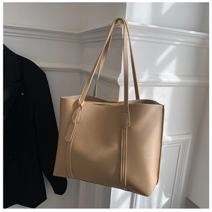 Khaki soft leather tote bag hanging next to a black blazer against a white wall