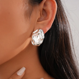 Close-up of irregular liquid silver metal stud earrings on a model with lava texture