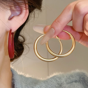 Close-up of model wearing large C-shaped metal hoops in gold and burgundy matte finish