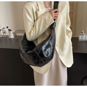 Detail of black crescent crossbody bag in glossy leather worn by a model in a cafe