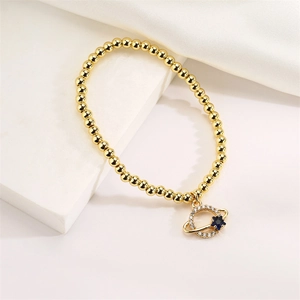 Detail of gold beaded bracelet featuring a Saturn charm with blue and white crystals