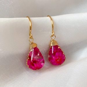 Close-up of handmade resin teardrop earrings with pink dried flowers and gold wire