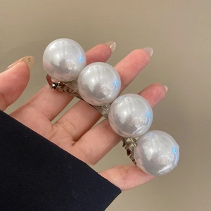 Detail showing four large white pearls on a silver spring hair clip held by hand