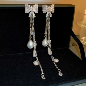 Detail of silver bow earrings with long tassels, rhinestones, and hanging drop pearls