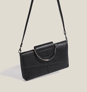 Detail of black patchwork handbag with snake texture and semi-circular metal handle