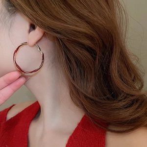 Close-up of wavy gold and red enamel earrings worn by a model in a minimal setting