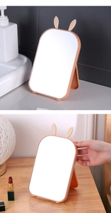 Detail view of foldable orange vanity mirror with rabbit ears on bathroom and wooden desks