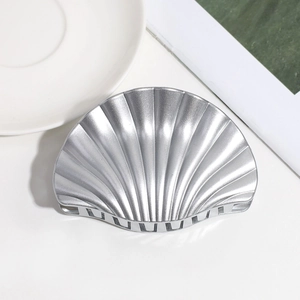 Close-up of a silver shell-shaped hair claw clip with metallic texture on white surface
