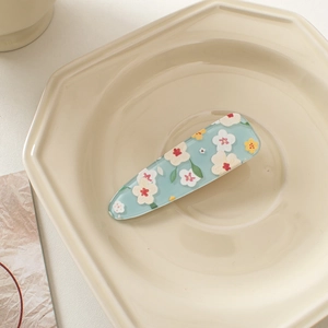 Detail view of light blue acrylic flower hair clip on a beige octagon tray