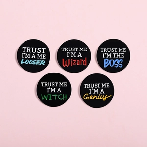 Set of five black enamel pins with slogans on a pink background, overhead view